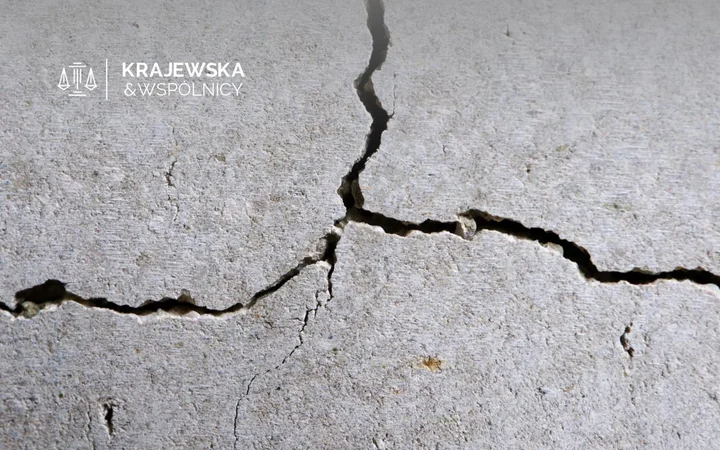 Spękana betonowa ściana z logo Krajewska & Wspólnicy