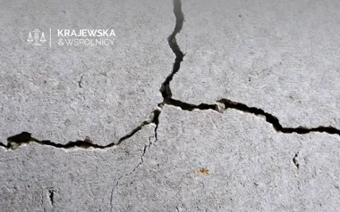 Spękana betonowa ściana z logo Krajewska & Wspólnicy
