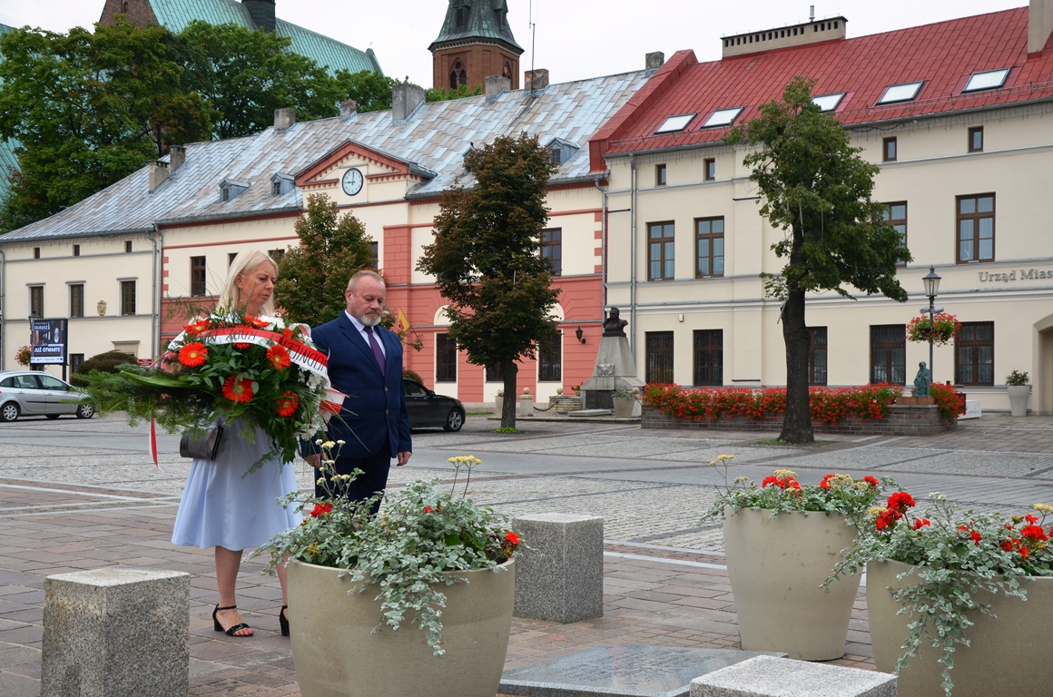 Kobieta i mężczyzna składają kwiaty pod pomnikiem na rynku