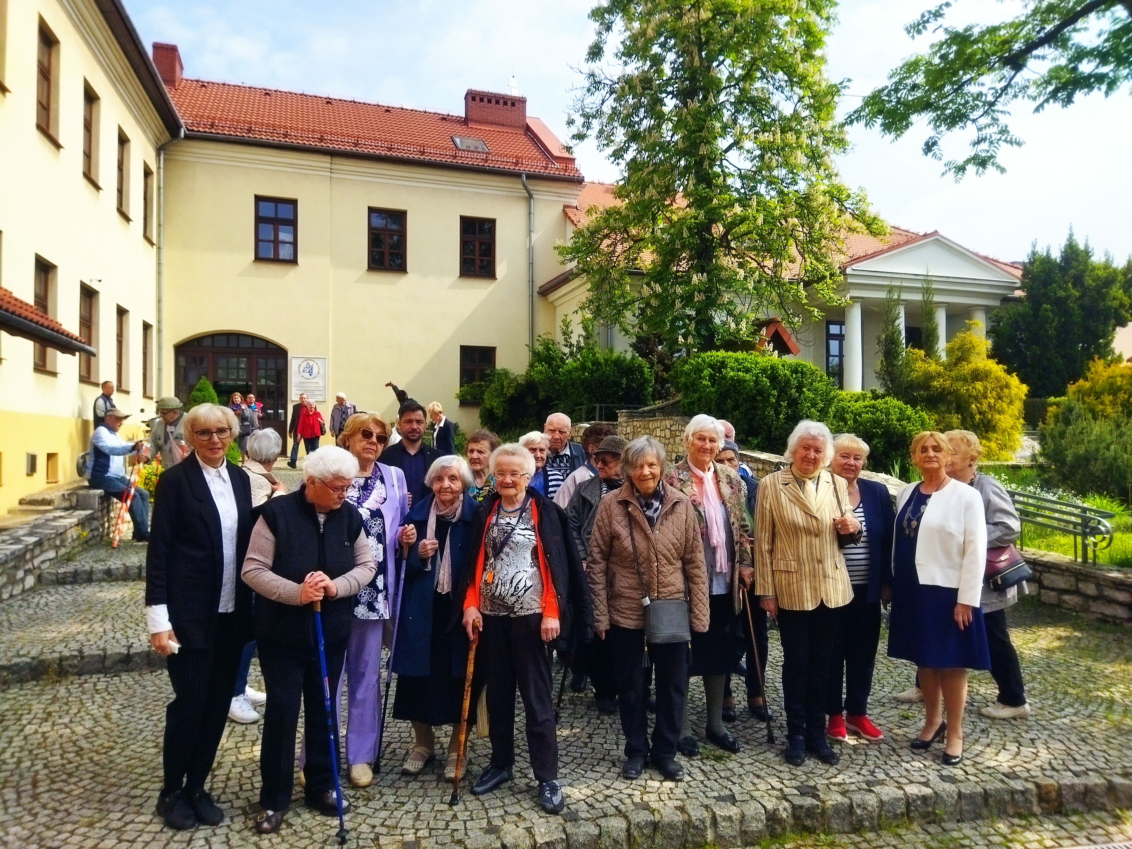 Kilkanaście starszych osób stoi przed zabytkowym budynkiem