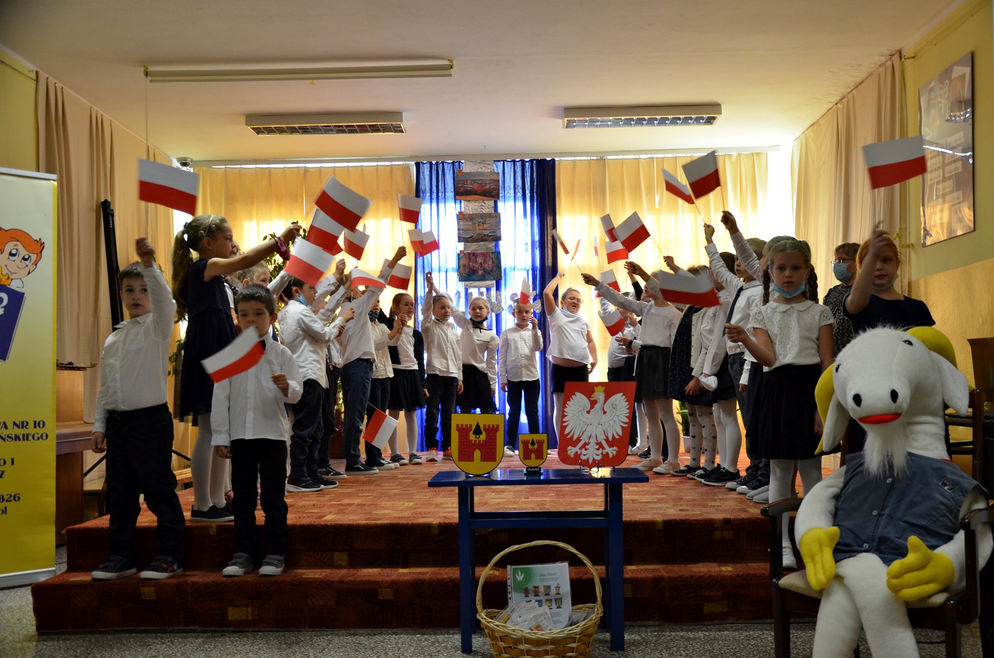 Grupa uczniów stoi na scenie z flagami