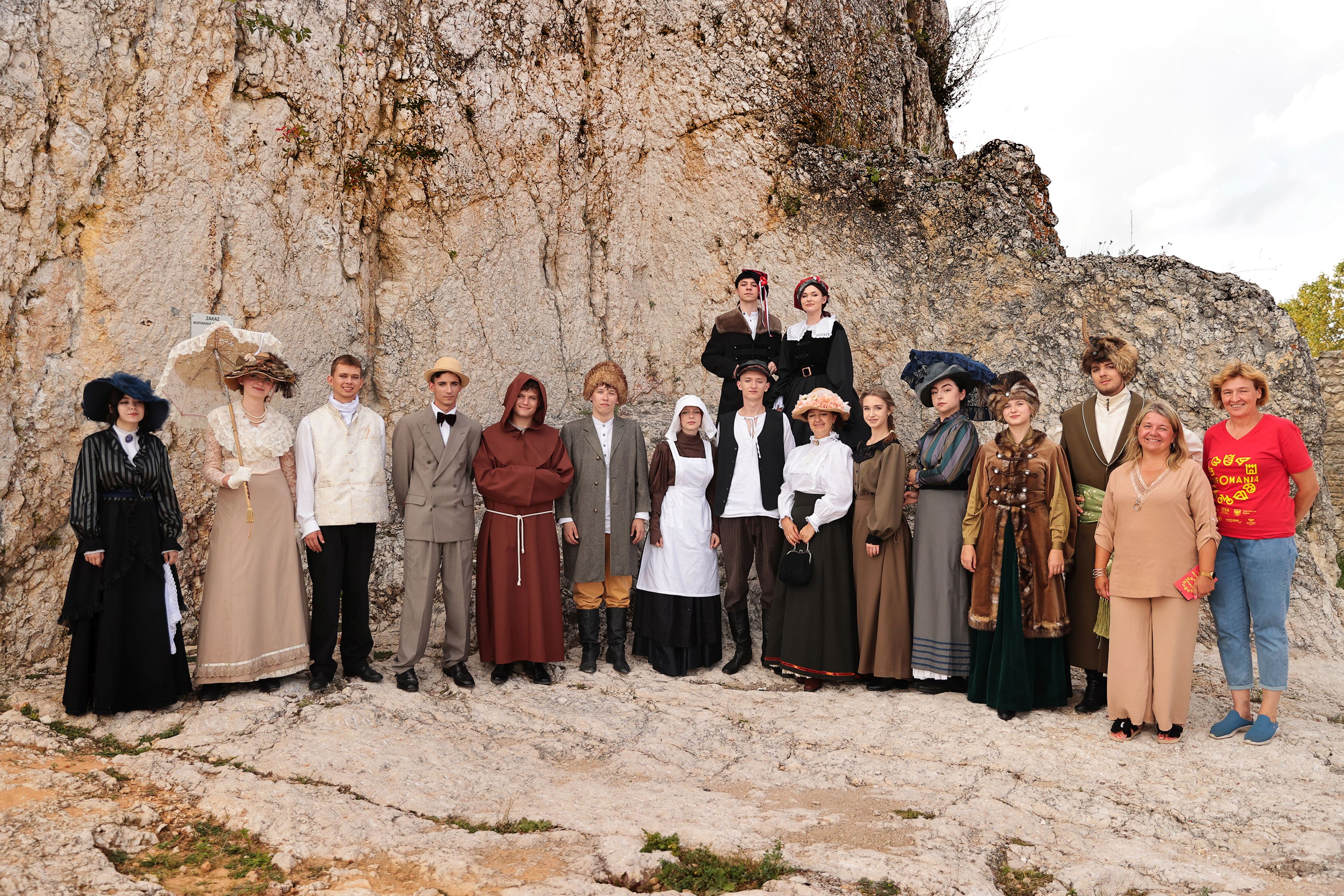Grupa osób ubranych w stroje historyczne stoi na tle białej skały