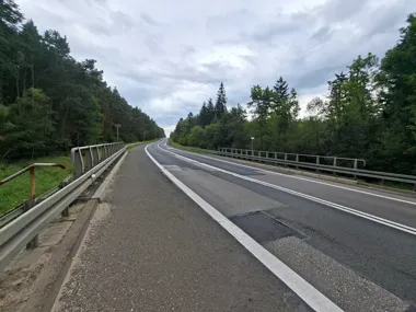 Droga krajowa prowadząca przez most otoczony lasem, widok w kierunku jadących pojazdów pod zachmurzonym niebem.